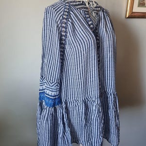May include: A blue and white striped dress with long sleeves and a ruffled hem. The dress is displayed on a white wire dress form. The sleeves have blue embroidered details.
