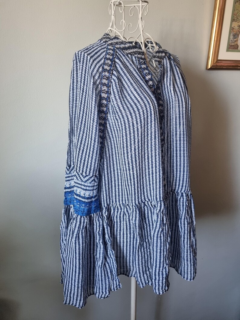 May include: A blue and white striped dress with long sleeves and a ruffled hem. The dress is displayed on a white wire dress form. The sleeves have blue embroidered details.