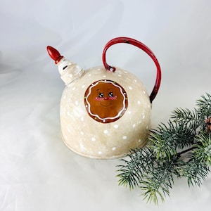 May include: A whimsical, cream-colored teapot with a red handle and spout. The teapot is decorated with white polka dots and a gingerbread man face. A festive holiday decoration.
