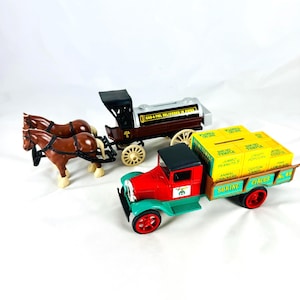 May include: A collection of vintage toy vehicles, including a red and green truck with "Shrine Circus No. 49" text, a brown horse-drawn carriage, and a brown truck with "Gas-A Fuel Delivered in Piper" text.