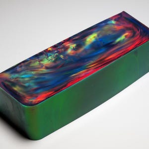 Peut inclure: Un bloc rectangulaire avec un motif tourbillonnant de couleurs vives, notamment le rouge, le bleu, le jaune et le vert. Les côtés du bloc sont d'un vert profond uni. La surface supérieure est brillante.