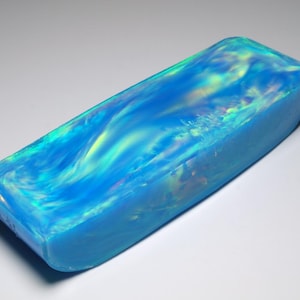Peut inclure: Un bloc rectangulaire en résine présentant un motif tourbillonnant de teintes bleu vif, turquoise et jaune irisé. La surface possède une finition lisse et polie avec une qualité semi-translucide qui crée une profondeur de couleur et de lumière.