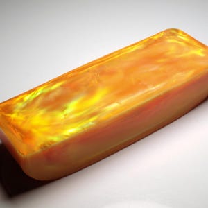 Peut inclure: Un objet rectangulaire de couleur ambre avec un intérieur marbré et lumineux. Le matériau translucide présente un motif flamboyant jaune et orange, et les bords sont arrondis. L'objet projette une ombre sur la surface blanche.