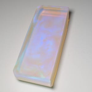 Peut inclure: Un plateau rectangulaire doté d'une surface lisse et translucide présentant une finition irisée et opalescente. Le matériau alterne entre des nuances douces de bleu pâle, de rose clair et de blanc crème, créant un effet nuageux et tourbillonnant sur la base plate et les bords surélevés.