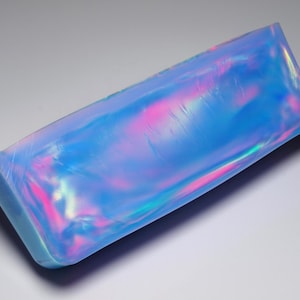 Peut inclure: Un grand opale bleu irisé de forme rectangulaire. L'opale a une surface lisse et polie et une légère courbure. L'opale est de couleur bleu clair avec des nuances de rose et de vert.