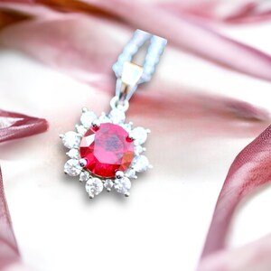 May include: A silver pendant necklace featuring a large red gemstone surrounded by smaller clear gemstones.