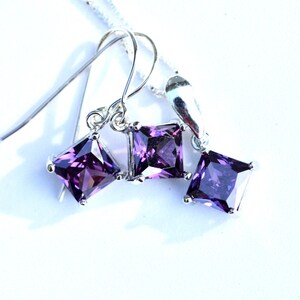 May include: A silver necklace and earrings set with three square-shaped purple gemstones.