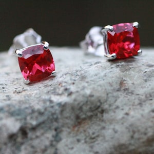 May include: A pair of silver earrings with red square-shaped gemstones.