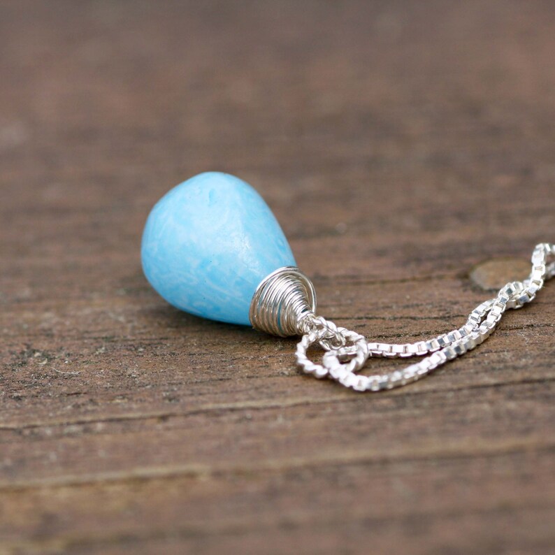 May include: A light blue gemstone pendant on a silver chain. The gemstone is wrapped in silver wire.
