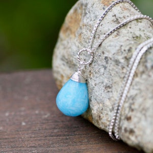 May include: A silver chain necklace with a light blue teardrop-shaped pendant. The pendant is wrapped in silver wire.