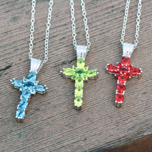 Puede incluir: Tres collares de plata con colgantes en forma de cruz. Las cruces están adornadas con piedras preciosas azules, verdes y rojas.