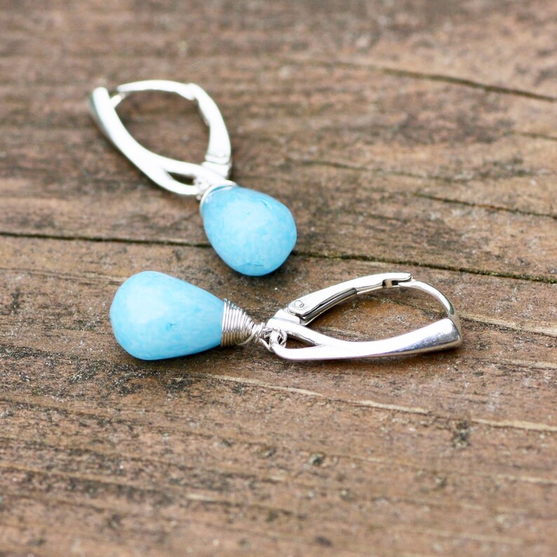 May include: A pair of silver teardrop earrings with light blue gemstone accents. The earrings have a wire-wrapped design and a leverback closure.