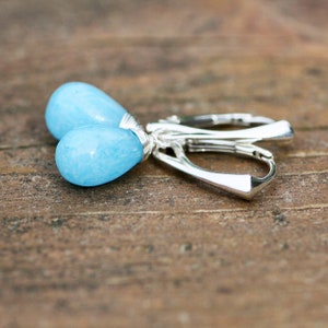 May include: A pair of silver earrings with light blue teardrop-shaped stones. The stones have a marbled pattern.