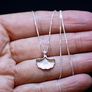 May include: A silver chain necklace with a delicate ginkgo leaf pendant. The pendant is textured and has a slightly rounded shape.