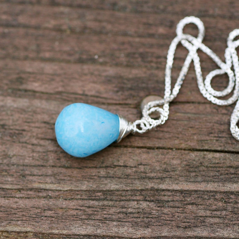 May include: A silver chain necklace with a light blue teardrop-shaped pendant.