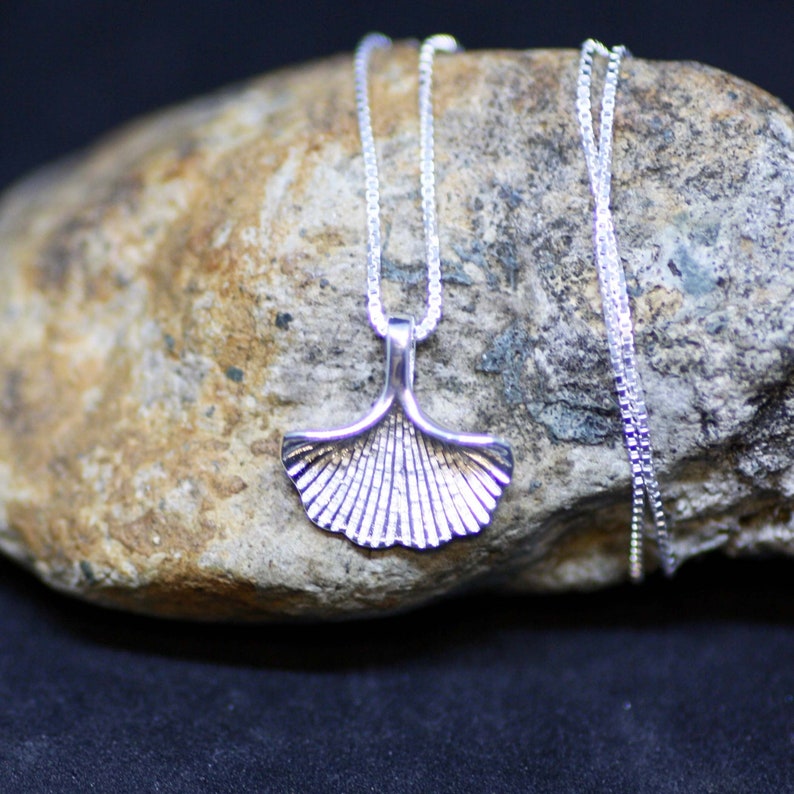 May include: A silver chain necklace with a ginkgo leaf pendant. The pendant is detailed with a textured surface.