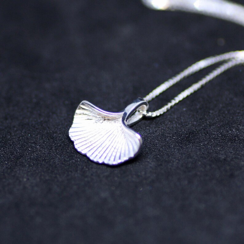 May include: A silver necklace featuring a ginkgo leaf pendant. The pendant is detailed with fine lines and has a delicate, feminine design.