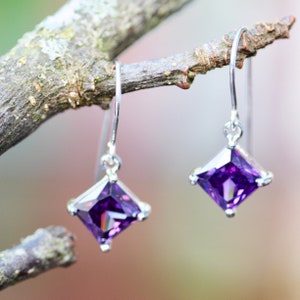 May include: A pair of silver earrings with square-shaped purple gemstones.