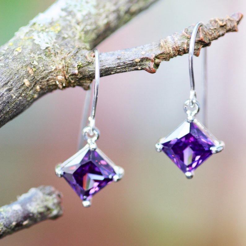 May include: A pair of silver earrings with square-shaped purple gemstones.