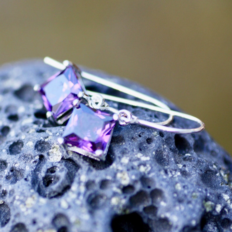 May include: A pair of silver dangle earrings with square purple amethyst gemstones.