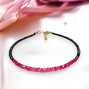 May include: A delicate bracelet featuring black and pink gemstones. The bracelet is made of small, faceted beads and has a gold clasp.
