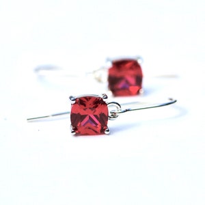 May include: A pair of silver dangle earrings with red square-shaped gemstones.