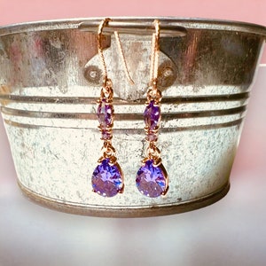 Peut inclure: Une paire de boucles d'oreilles pendantes dorées avec des cristaux violets en forme de goutte.