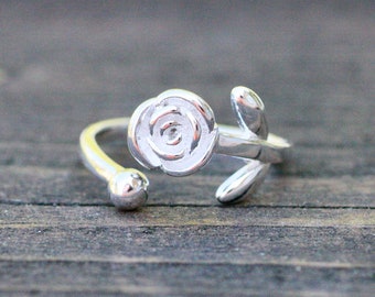 May include: A silver adjustable ring featuring a rose design. The rose is detailed with a swirl pattern and a stem with leaves.