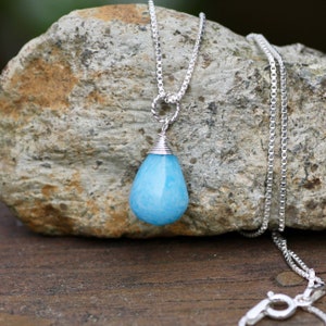 May include: A silver chain necklace with a light blue teardrop-shaped pendant. The pendant is made of a translucent stone with white swirls.