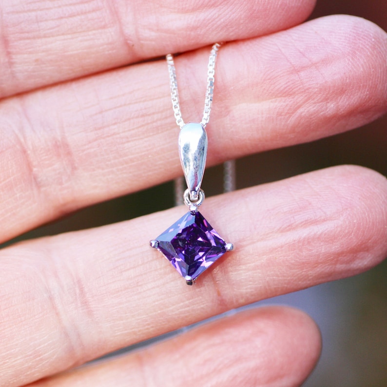 May include: A silver chain necklace with a square-shaped pendant featuring a large, dark purple gemstone.