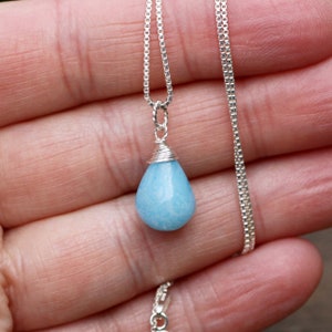 May include: A silver chain necklace with a teardrop-shaped blue aquamarine pendant.