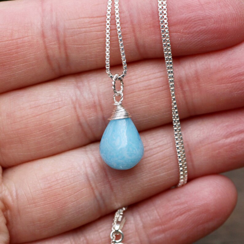 May include: A silver chain necklace with a teardrop-shaped blue aquamarine pendant.