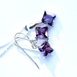 May include: A set of silver earrings and a necklace with purple square-shaped gemstones.