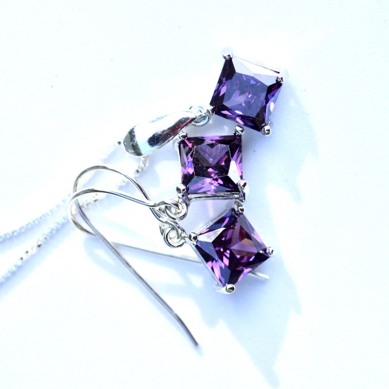 May include: A set of silver earrings and a necklace with purple square-shaped gemstones.