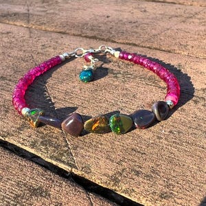 May include: A handmade bracelet with a bright pink beaded chain, silver accents, and a small charm. The bracelet includes polished gemstones in purple, brown, and green. The bracelet is designed to fit a wrist size of approximately 17 cm.