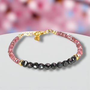 Peut inclure: Bracelet délicat avec des pierres roses et noires. La chaîne et le fermoir sont dorés. Les pierres roses sont petites et rondes, tandis que les pierres noires sont facettées. Un charm en forme de cœur est suspendu au fermoir.