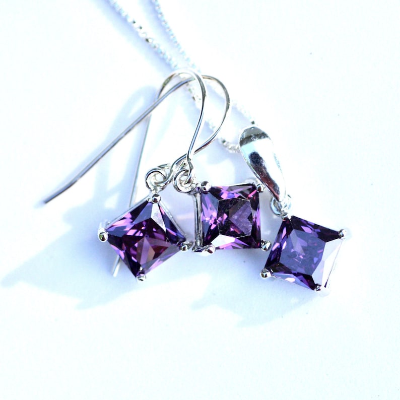 May include: A silver necklace and earrings set with three square-shaped purple gemstones.