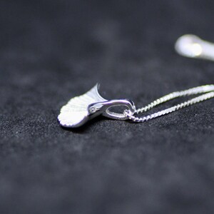 May include: A silver necklace featuring a delicate, fan-shaped pendant. The pendant is crafted from smooth, polished metal and has a gently curved form.