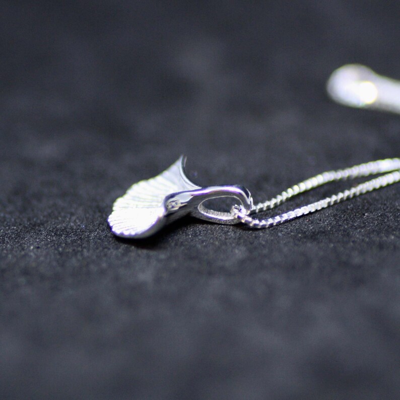 May include: A silver necklace featuring a delicate, fan-shaped pendant. The pendant is crafted from smooth, polished metal and has a gently curved form.