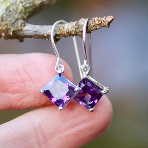 May include: A pair of silver earrings with square-shaped purple gemstones.