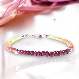 Puede incluir: Una delicada pulsera con una hilera de piedras preciosas facetadas de color rojo intenso, que transicionan a cuentas amarillas y naranjas. La pulsera está conectada por una cadena y un cierre de plata, creando un accesorio vibrante y elegante.