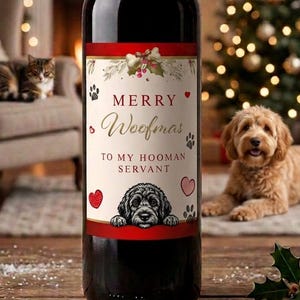 Pode incluir: Uma garrafa de vinho de vidro escuro com um rótulo creme com bordas vermelhas, ilustrações de azevinho, pegadas, corações e o texto Merry Woofmas TO MY HOOMAN SERVANT sobre uma ilustração em preto e branco de um rosto de cão.
