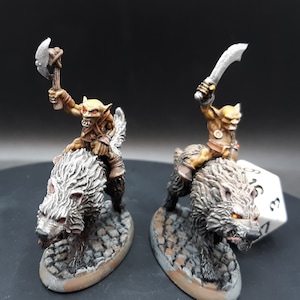 May include: Two miniature figurines of goblin riders on wolves. The goblins are painted with tan skin and brown clothing, wielding a battle axe and a curved sword. The wolves are gray with red eyes, mounted on stone bases.