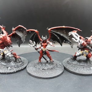 May include: Three miniature fantasy figures of demons with red skin, black wings, and horns. One figure holds a sword, another a trident, and the third a staff. They stand on gray circular bases, perfect for tabletop gaming or collecting.