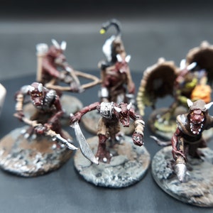 May include: A collection of hand-painted fantasy miniatures, featuring creatures with horns, claws, and weapons. The figures are in shades of red, brown, and gray, set on textured bases. A white die with black numbers is in the background.