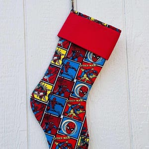May include: A festive Christmas stocking with a Spider-Man comic book design. The stocking has a red cuff and a loop for hanging. The main body of the stocking is patterned with comic book panels in red, blue, and yellow.
