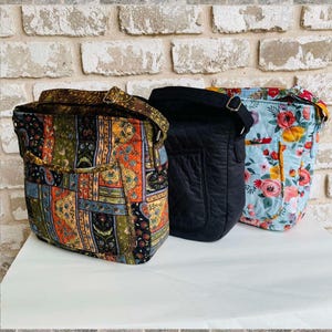May include: Three quilted shoulder bags. One is black, one is blue with a floral print, and one is multi-coloured with a paisley pattern.