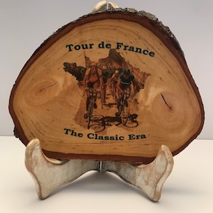 Puede incluir: Una placa de madera con una imagen impresa de ciclistas en el Tour de Francia. La placa está inscrita con las palabras "Tour de France" y "The Classic Era".