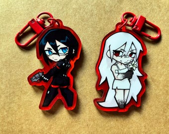 Könnte beinhalten: Zwei Schlüsselanhänger im Anime-Stil mit roten Rändern und Verschlüssen. Einer zeigt eine Figur in schwarzer Kleidung mit einer Waffe, der andere eine Figur in einem weißen Kleid, die Blumen hält. Beide haben ein cartoonartiges Design.