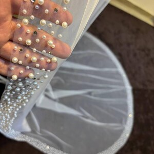 Peut inclure: Un voile de mari&eacute;e blanc orn&eacute; de fausses perles et de cristaux. Le bord du voile est &eacute;galement orn&eacute; de perles, cr&eacute;ant un design d&eacute;licat et &eacute;l&eacute;gant. Le voile est fait d'un tissu transparent et l&eacute;ger.